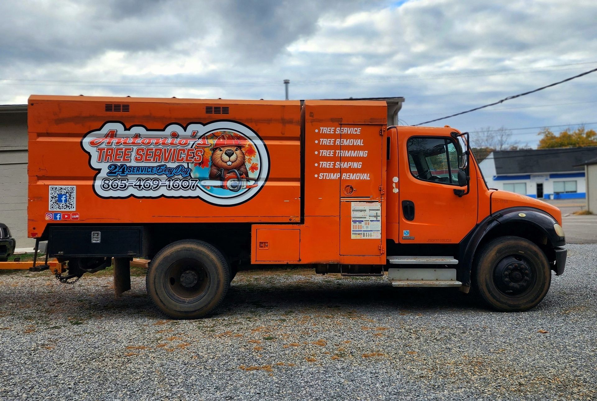 A large orange truck is parked in a gravel lot.