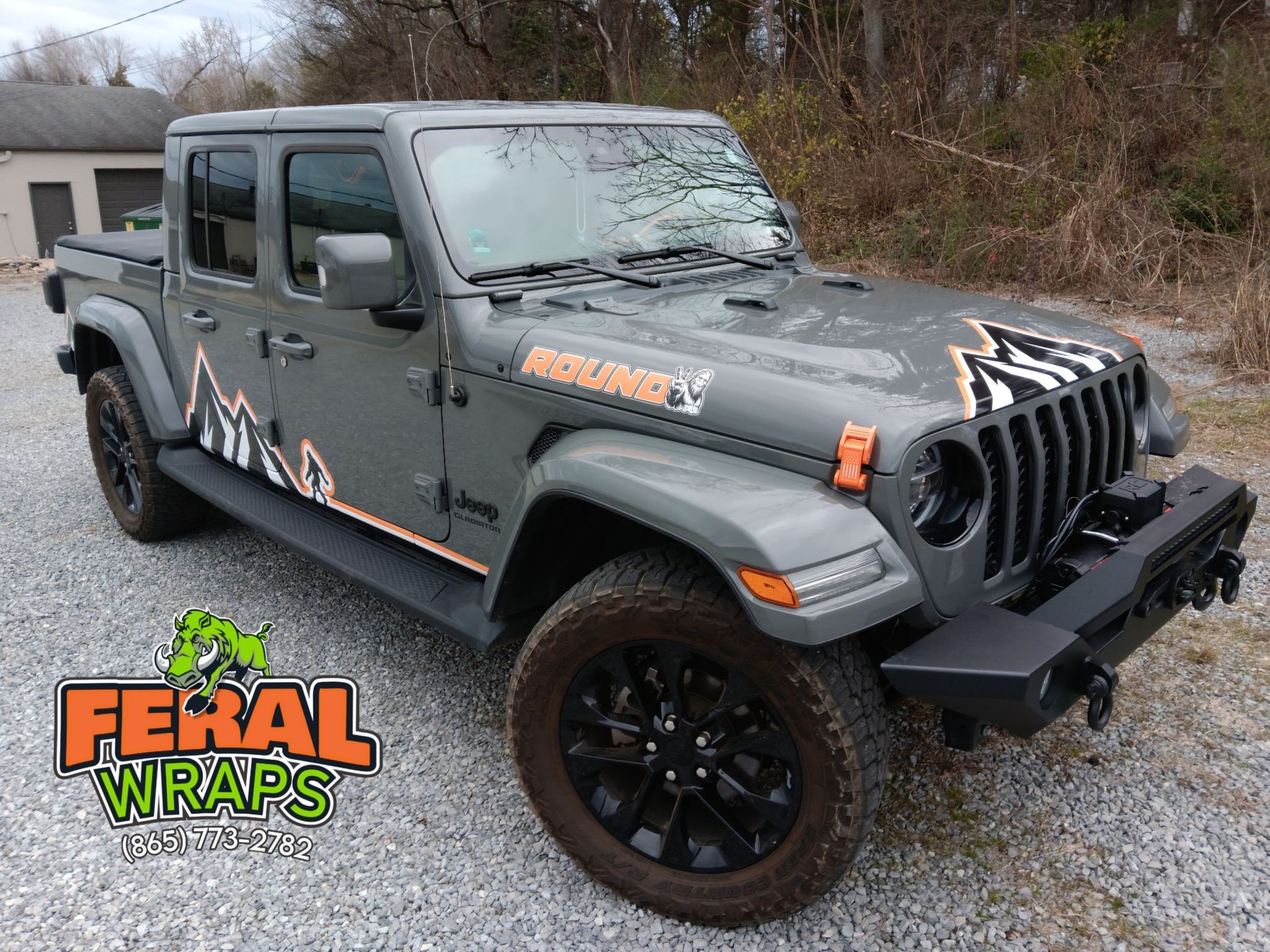 A gray jeep wrangler is parked in a gravel lot.