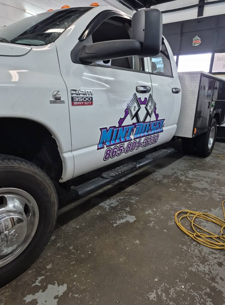 A white truck with a purple logo on the side is parked in a garage.