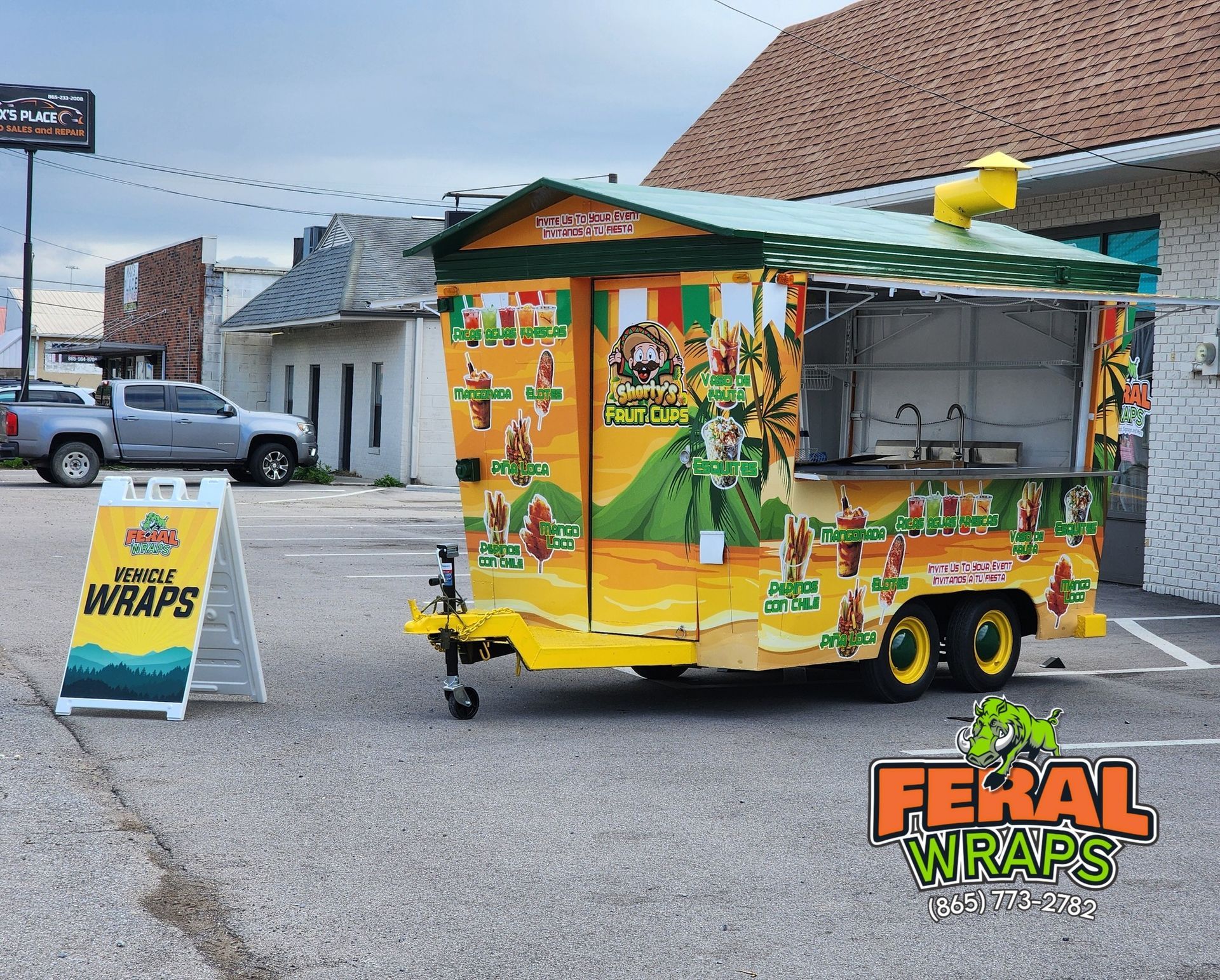 A food truck is parked in a parking lot next to a sign that says feral wraps.