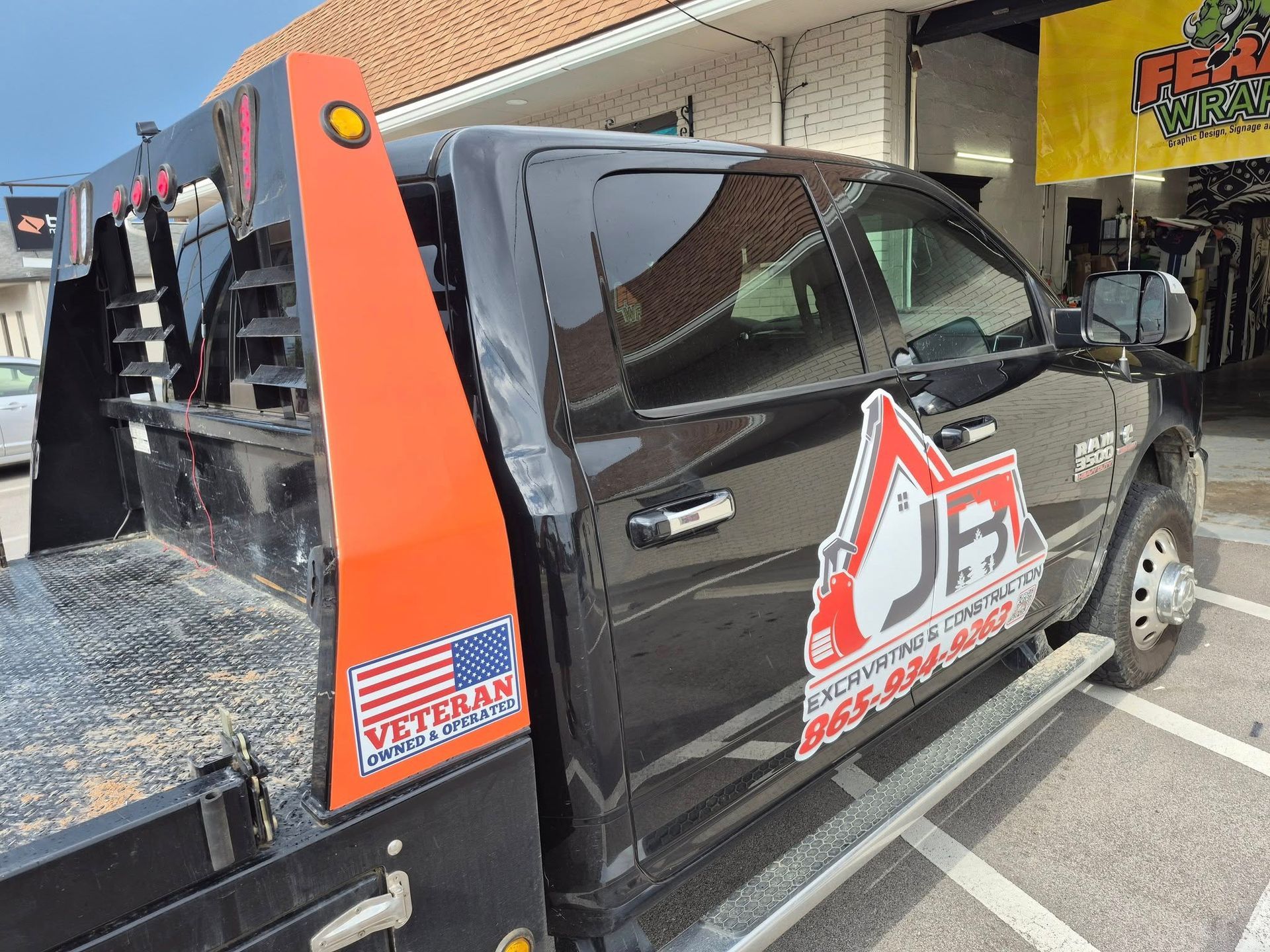 Black work truck with orange accents and veteran logo parked outside a shop.
