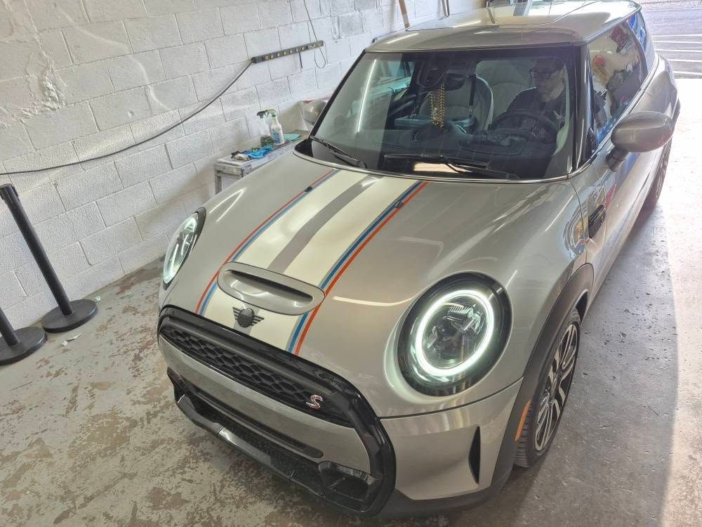 Silver Mini Cooper with racing stripes in a garage.