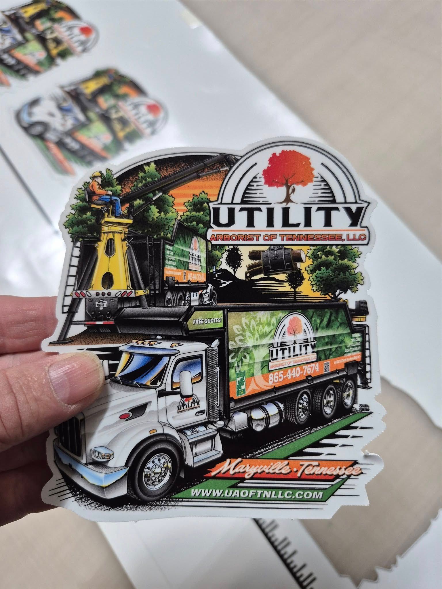 A hand holding a sticker of a utility truck with a tree, the logo says 