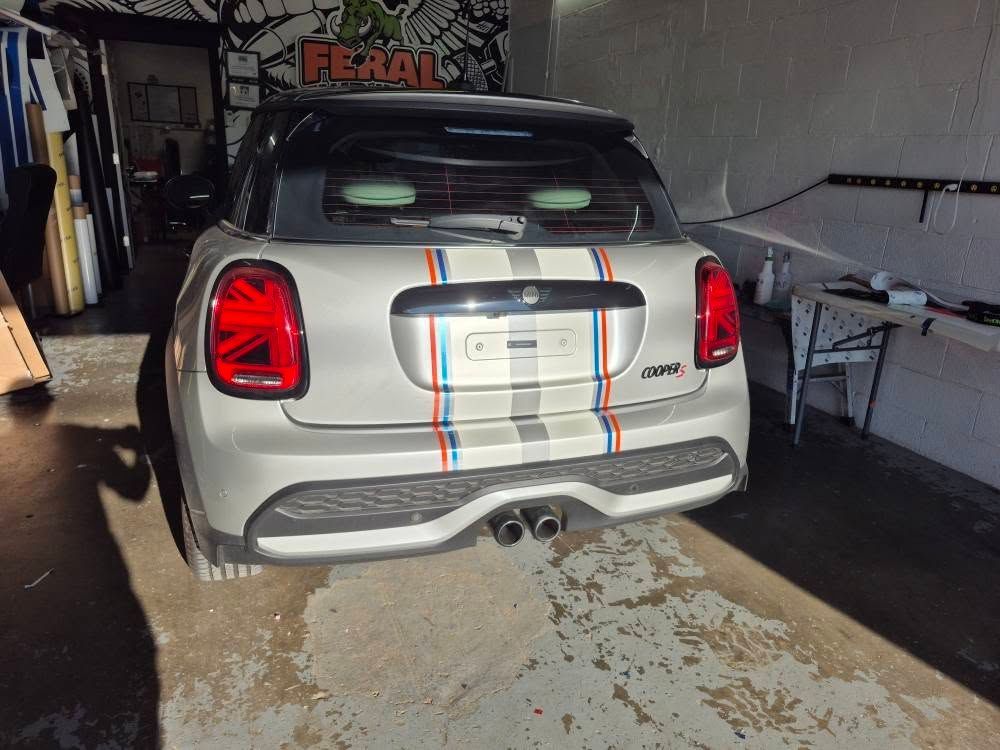 Silver Mini Cooper with racing stripes, parked in a garage.