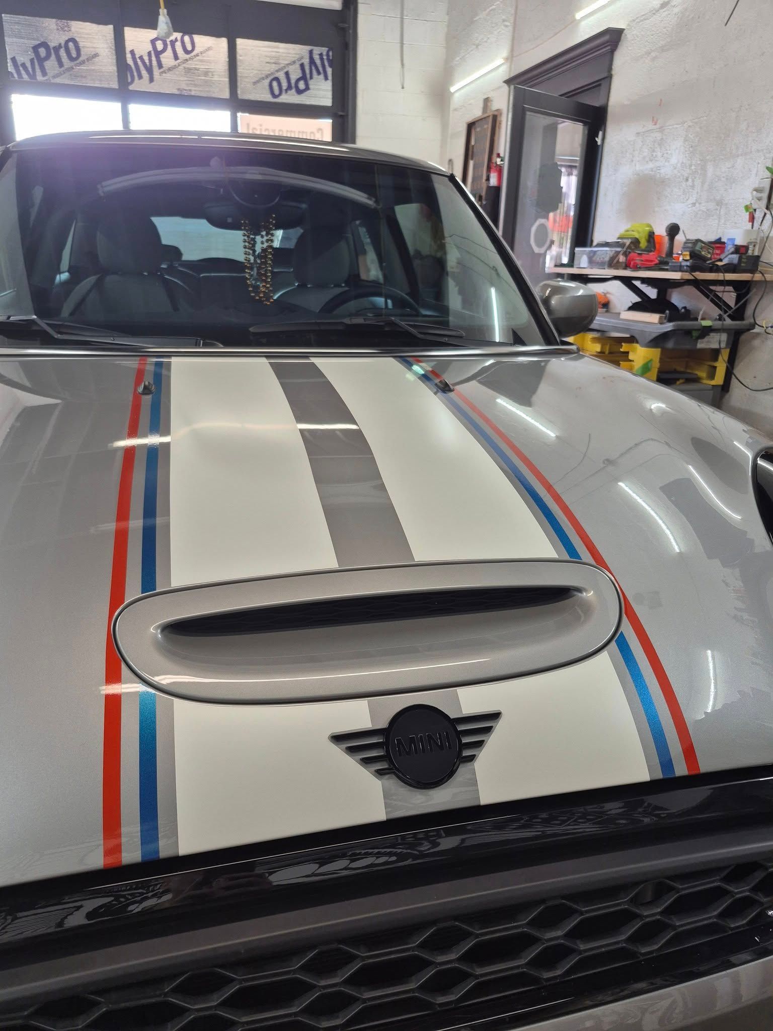 Silver Mini Cooper with colorful racing stripes on the hood, parked indoors.