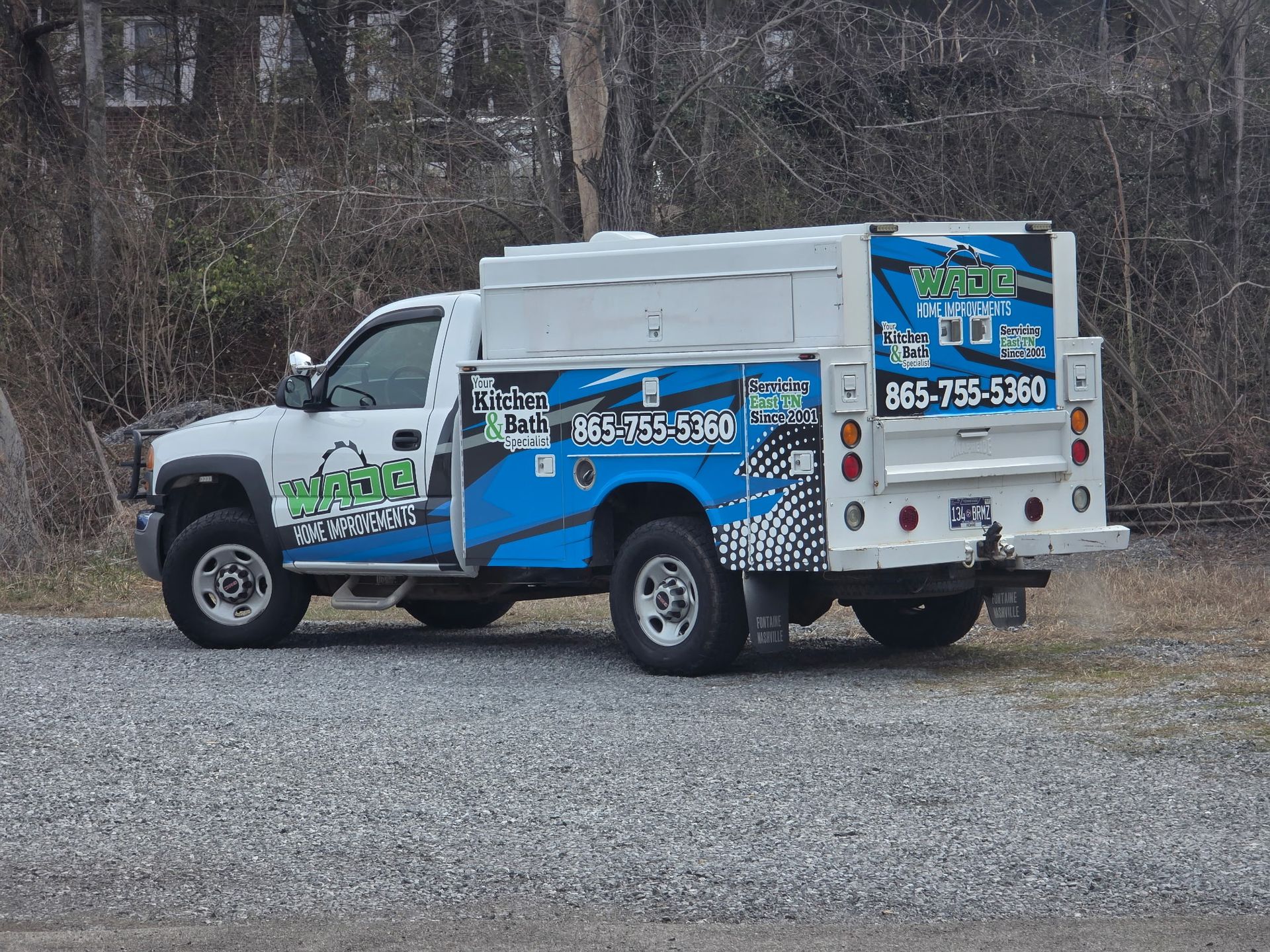 White and blue service truck with company logo and phone number parked on gravel.