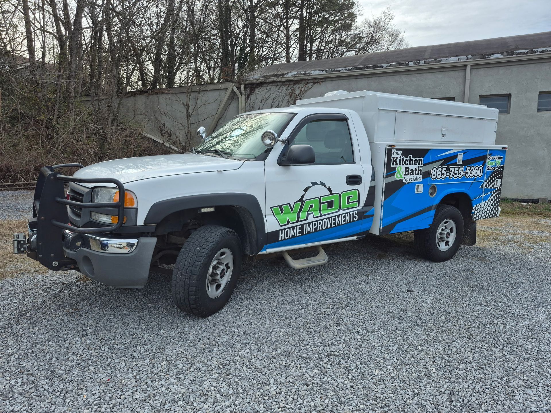 White work truck with blue and green graphics, parked on gravel.