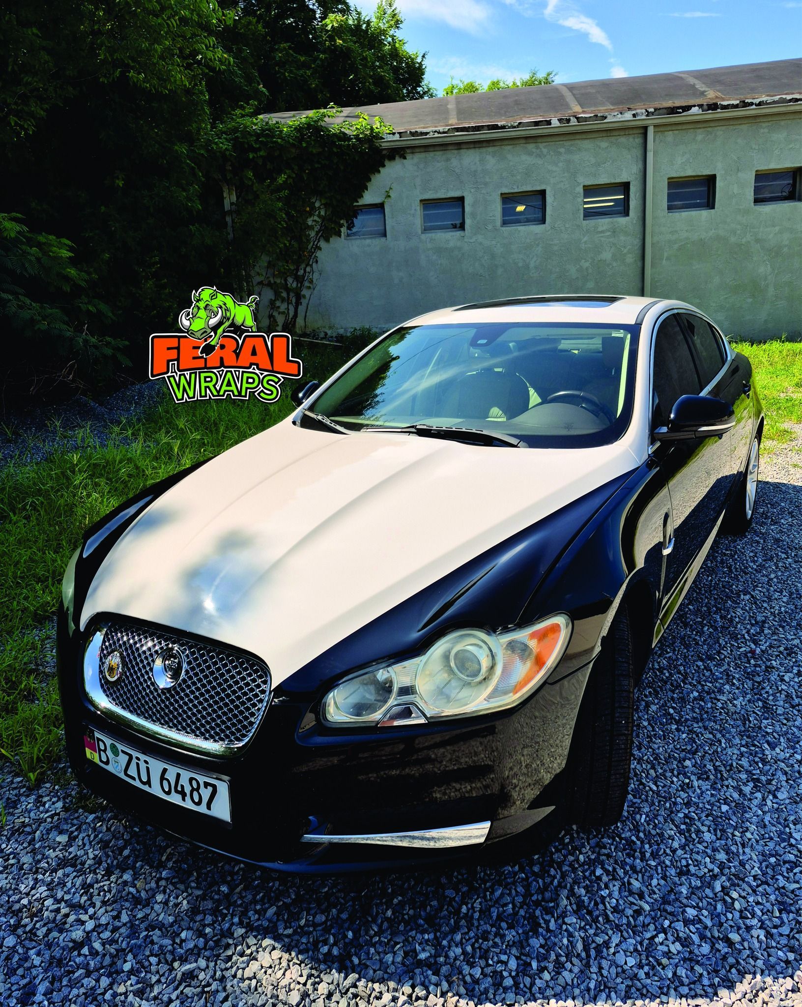 Two-tone Jaguar XF parked on gravel. A light-colored hood and roof contrast with the dark blue body. Building in background.