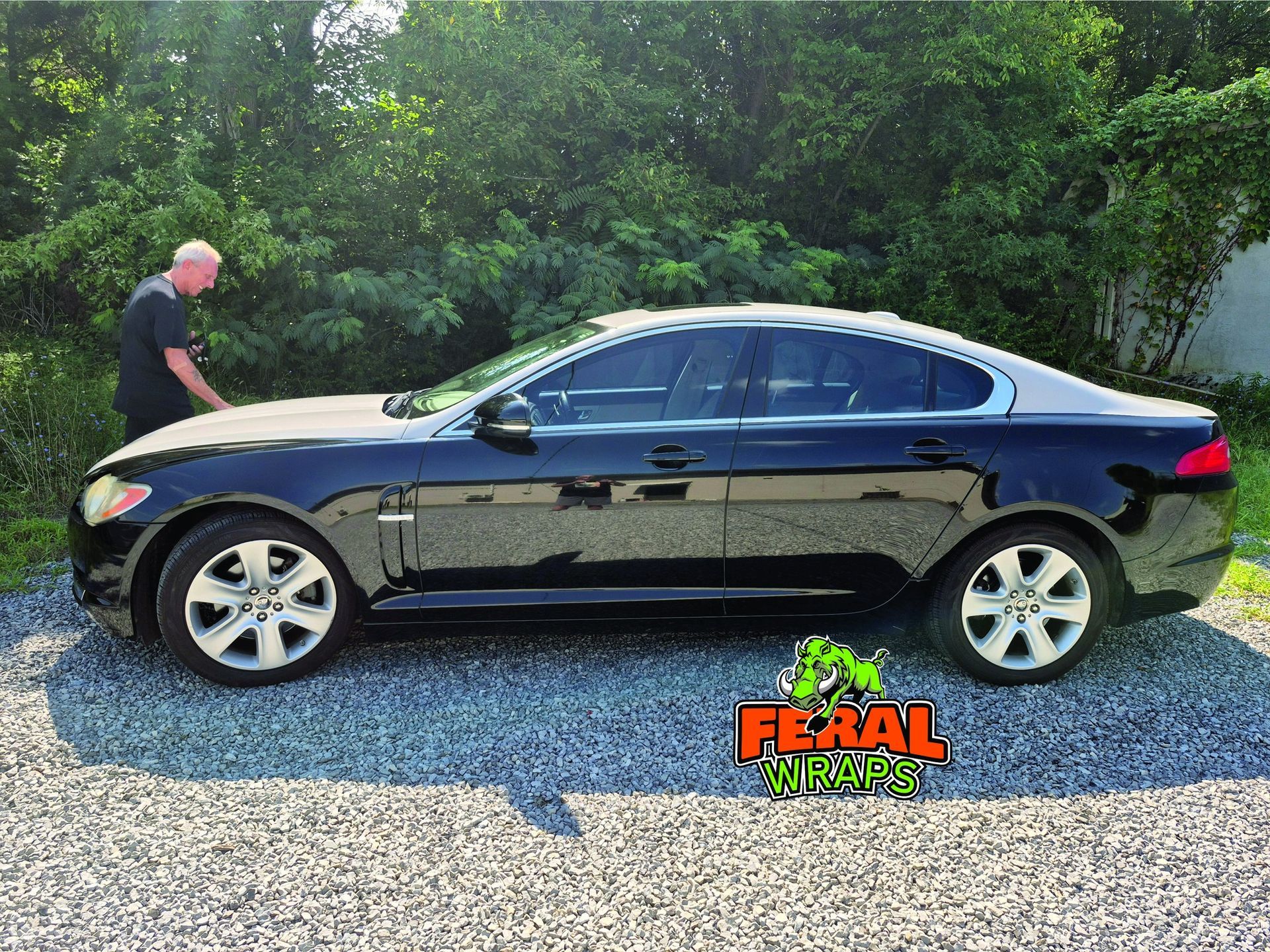 Black Jaguar sedan parked on gravel, man standing next to it.