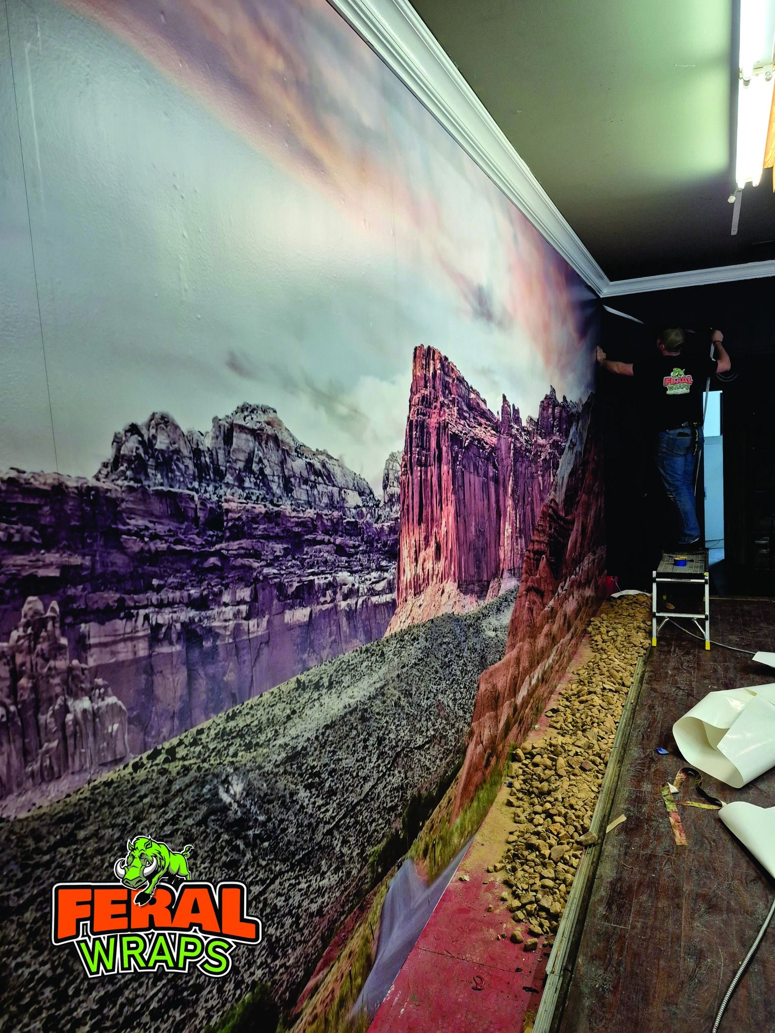 A person installing a large mural of a canyon landscape on a wall.