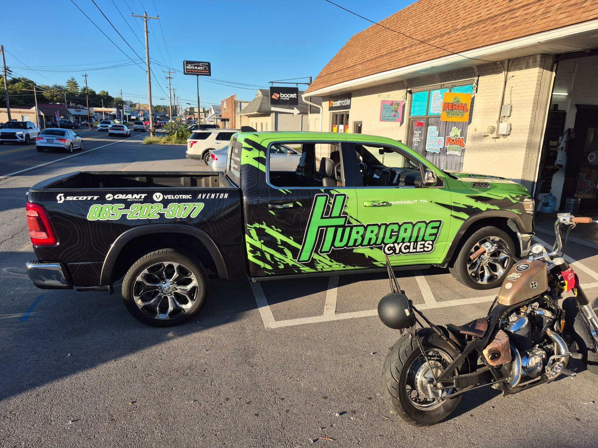 Black and green pickup truck with “Hurricane Cycles” logo parked outside a shop, motorcycle in foreground.