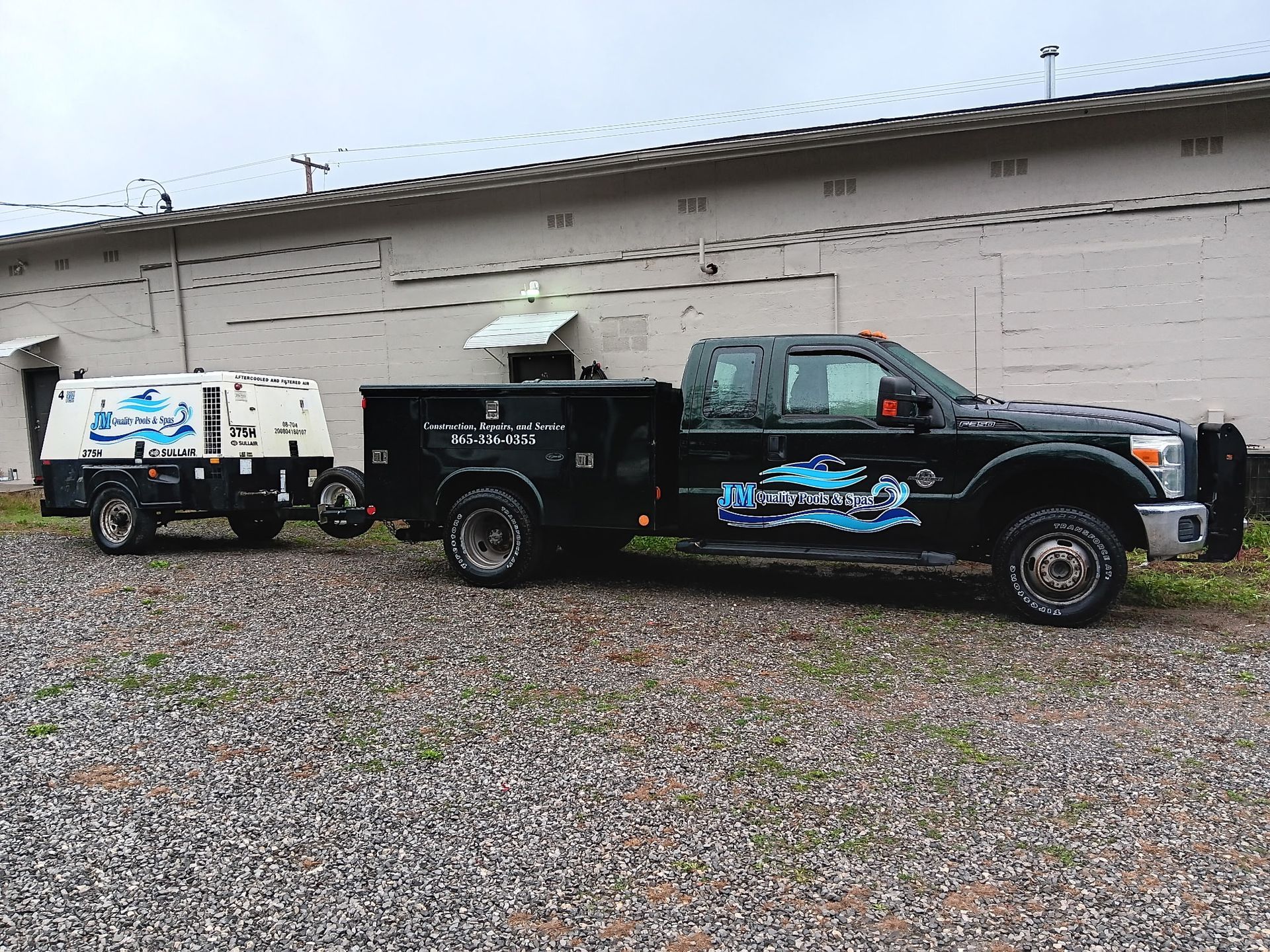 A truck with a trailer attached to it is parked in a gravel lot.
