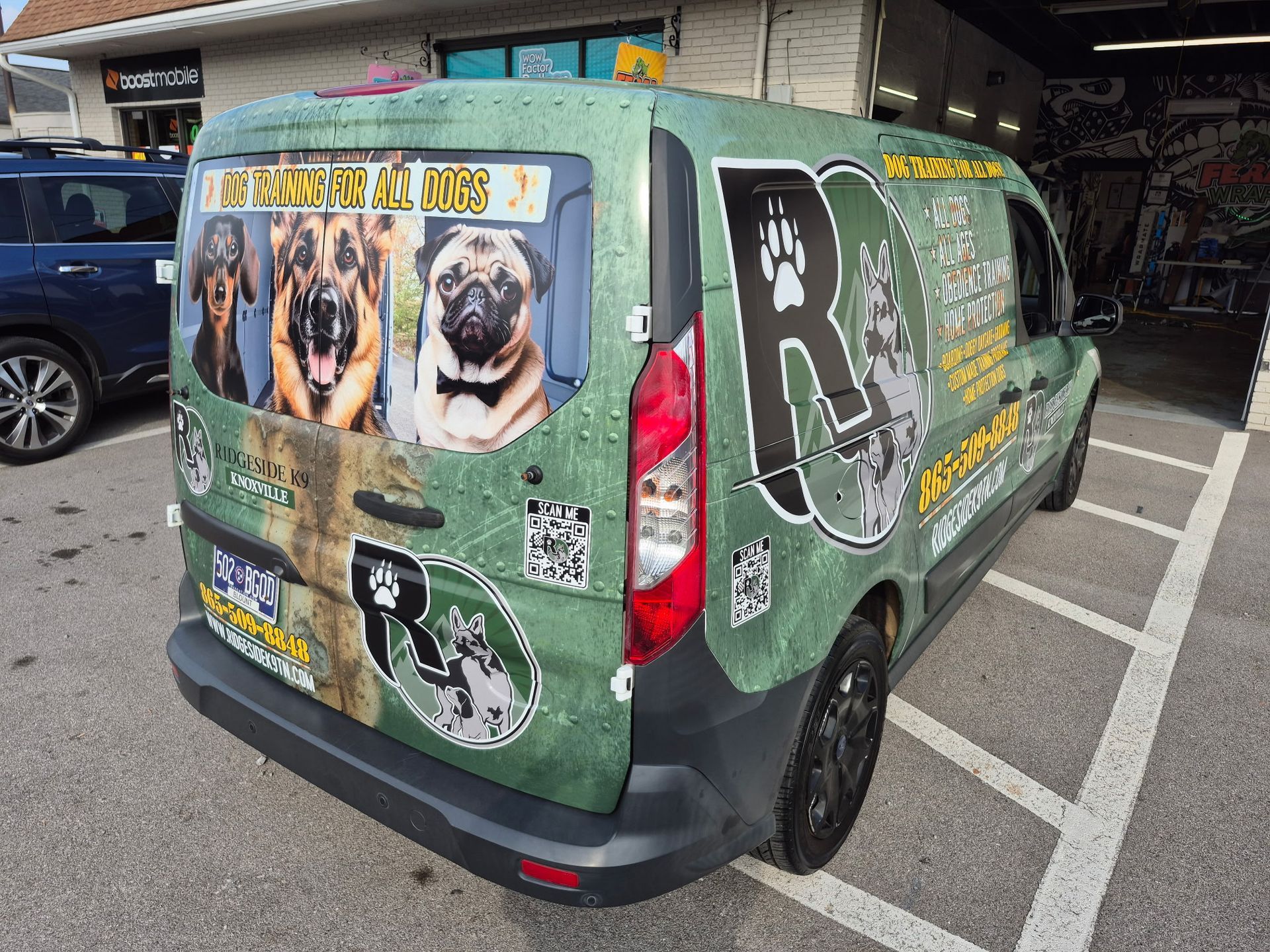 Green van with dog-themed graphics, parked in a lot, with a blue SUV nearby.