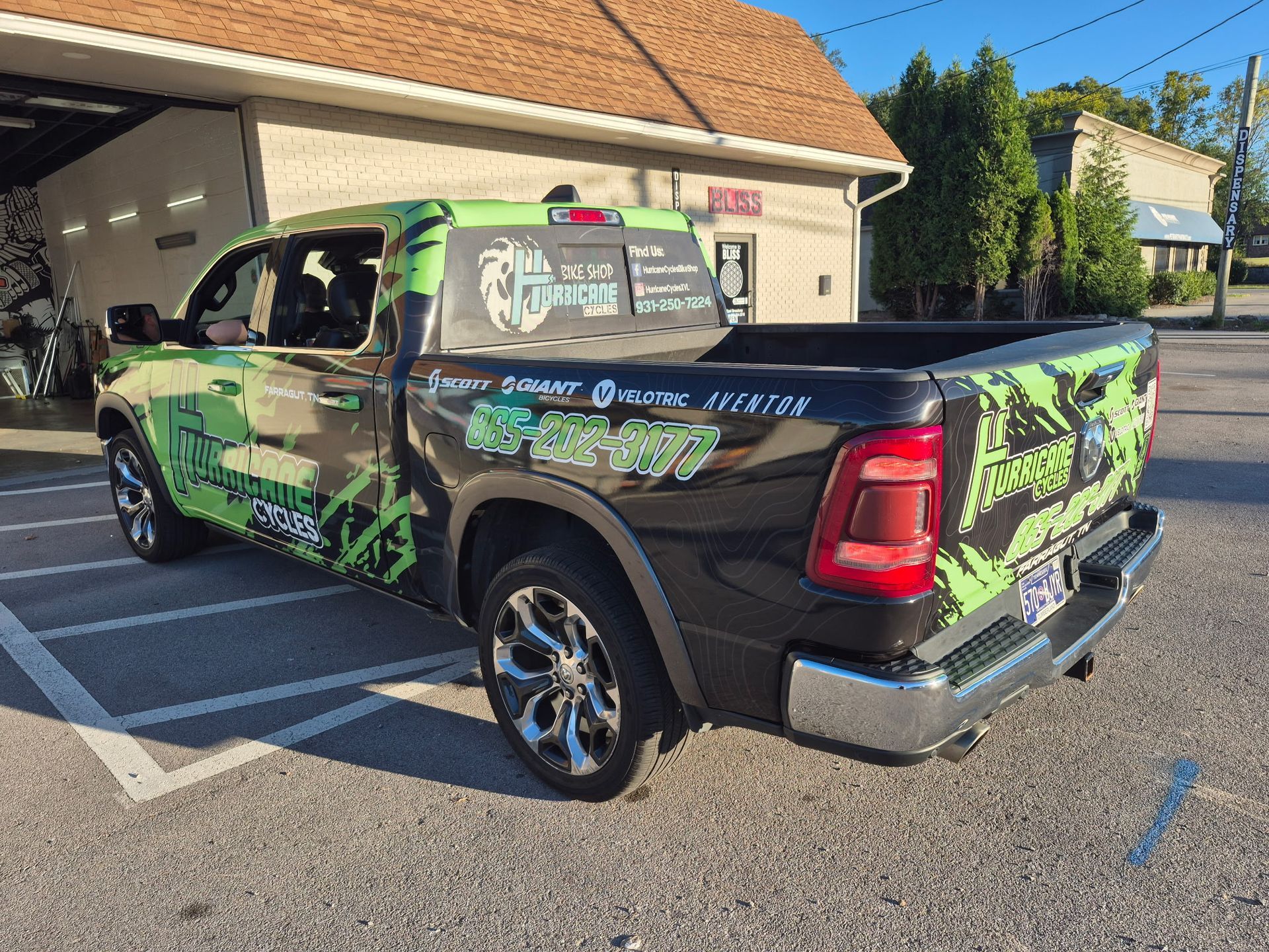 Black pickup truck with green graphics parked in front of a building on a sunny day.