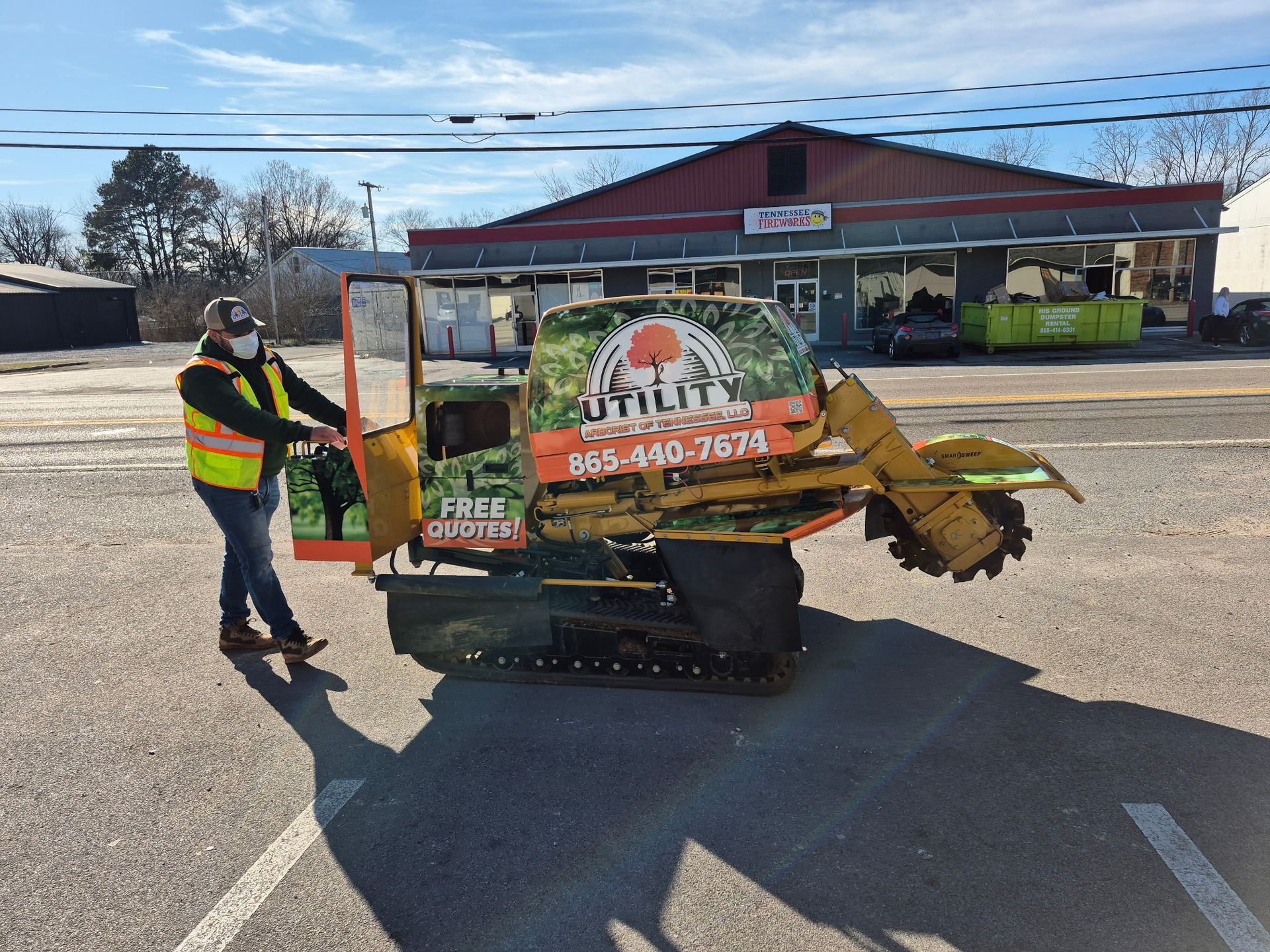 A man is standing next to a stump grinder in a parking lot.