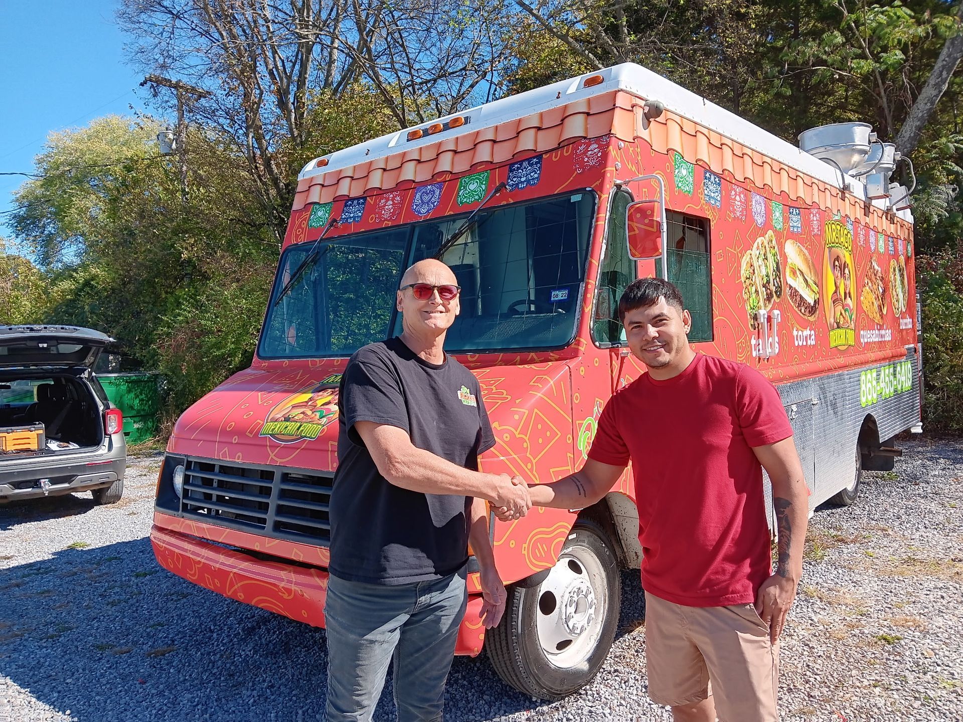Two men are shaking hands in front of a red food truck.
