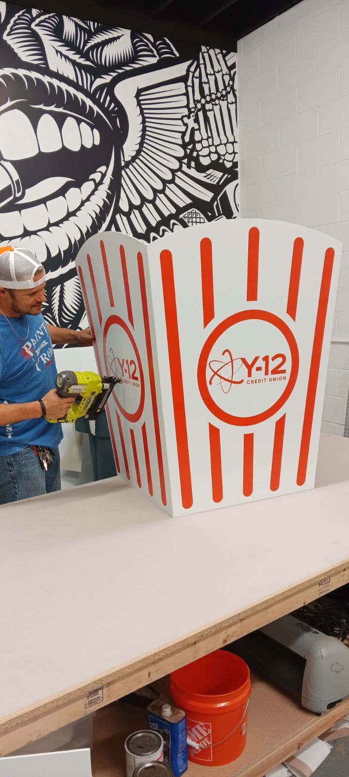 A man is holding a drill next to a large popcorn box.