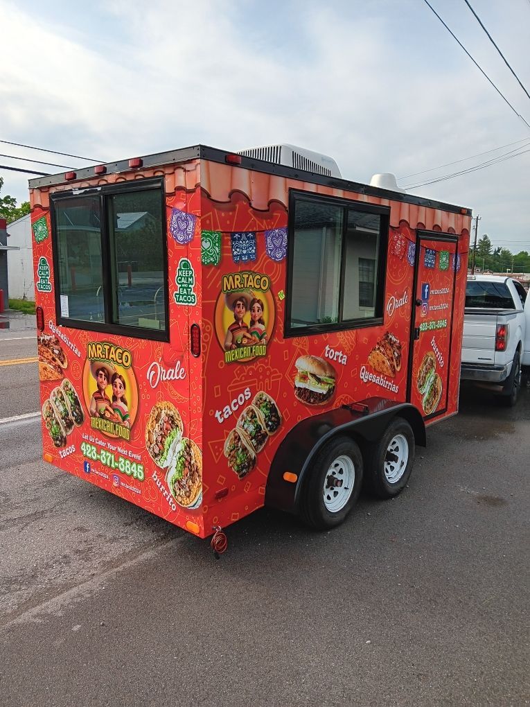 A red food truck is parked on the side of the road next to a truck.