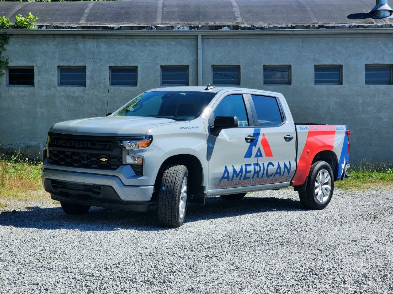 An american truck is parked in a gravel lot in front of a building.