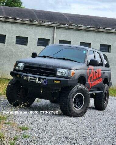 A black suv is parked in a gravel lot in front of a building.