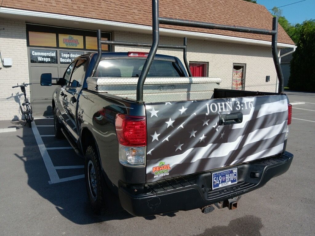 A black truck with an american flag on the back is parked in front of a building.
