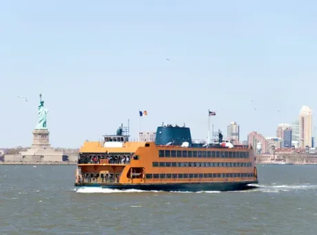 Orange Staten Island Ferry sails past the Statue of Liberty in New York City harbor.
