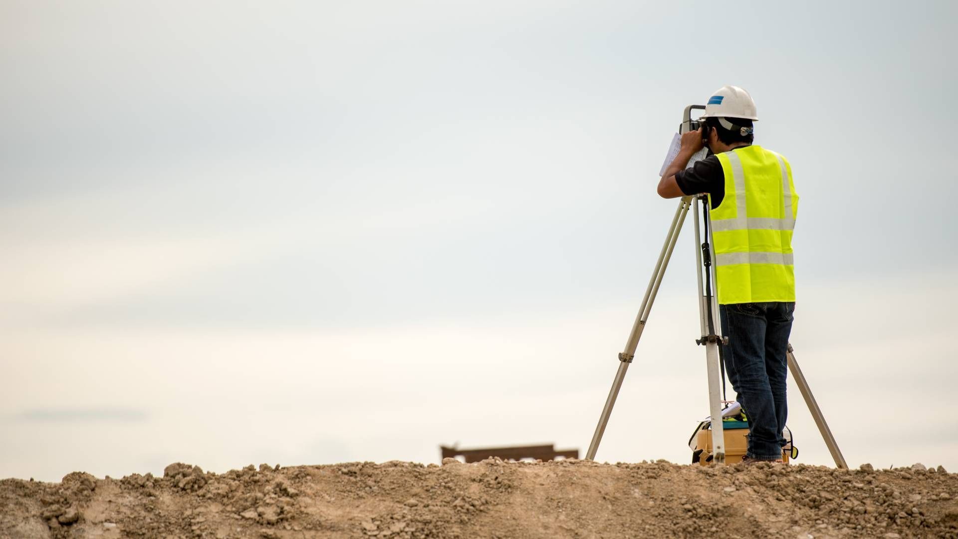 Surveyor in a yellow vest using surveying equipment on a construction site, surveying land.