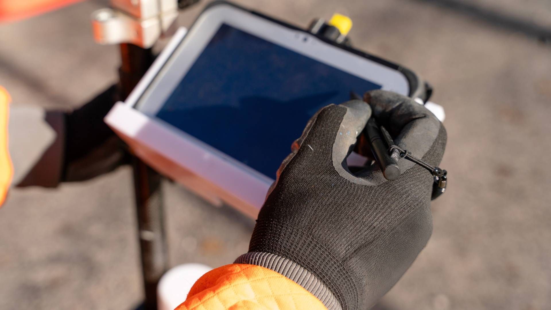 Person in black gloves uses a stylus on a tablet, mounted on a pole, outdoors.