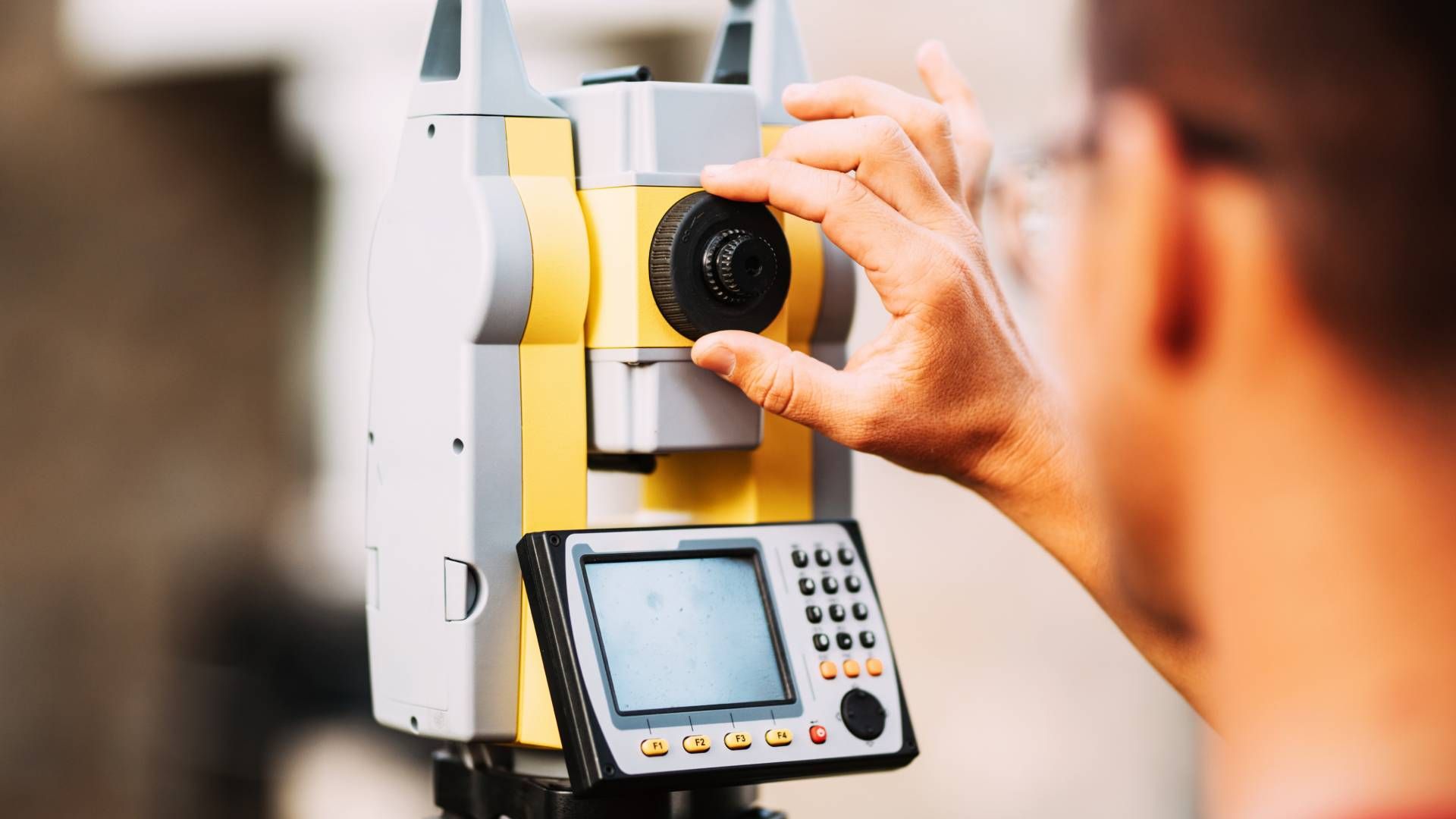 Man operating a yellow and gray surveying instrument, likely outdoors.