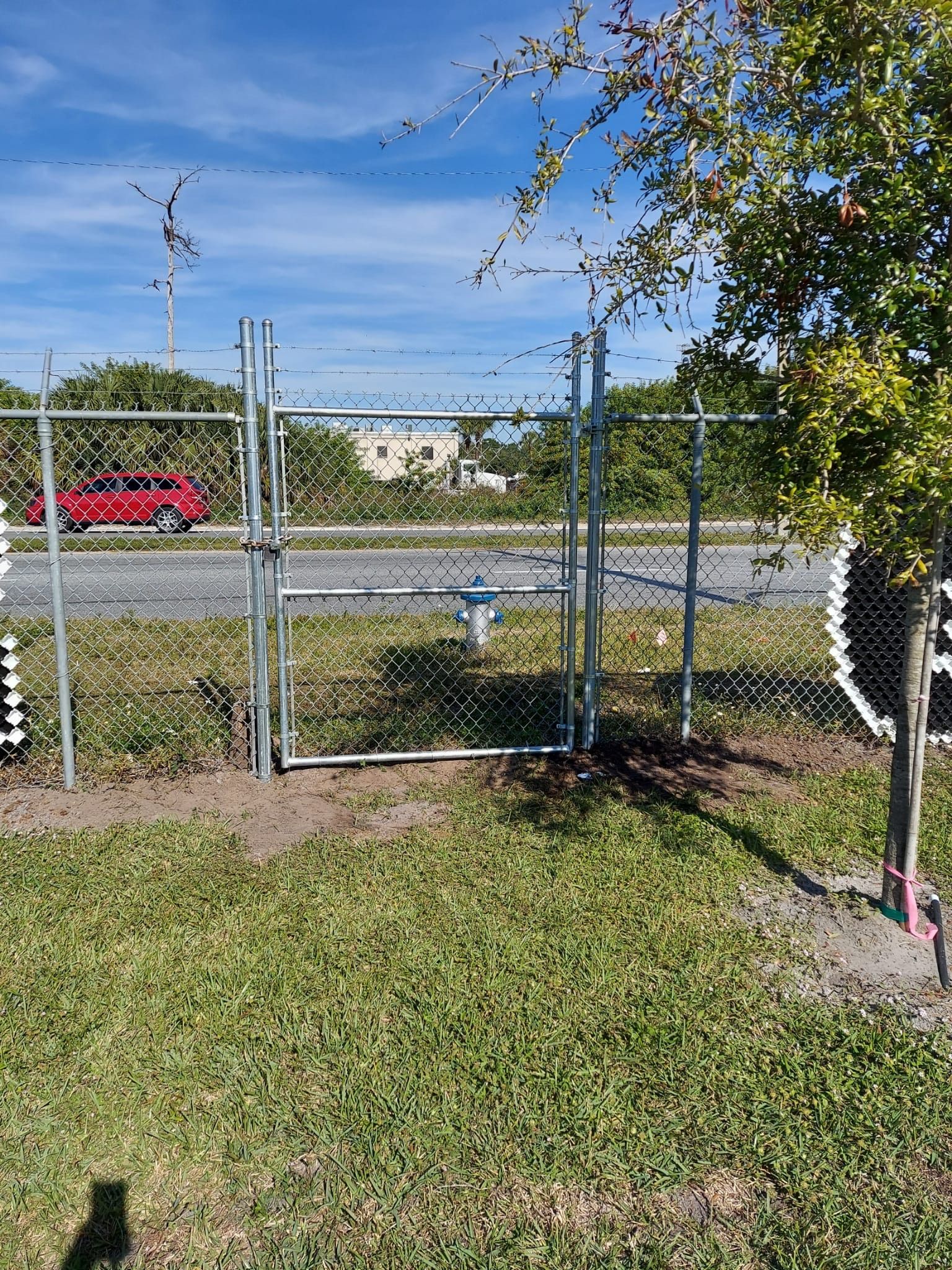 A chain link fence with a gate in the middle of a grassy field.