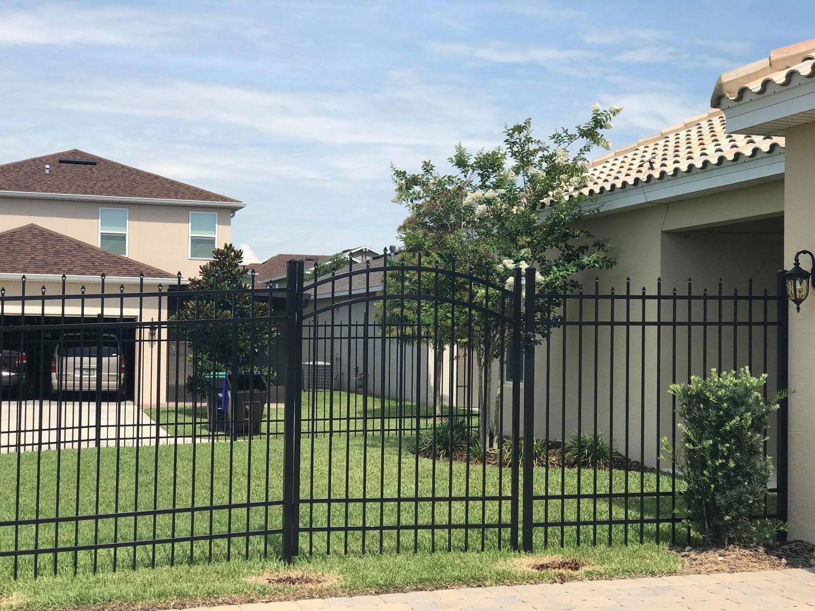 A black metal fence surrounds a lush green yard in front of a house.