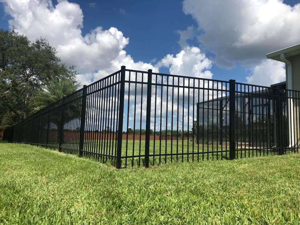 A black fence surrounds a lush green field in front of a house.