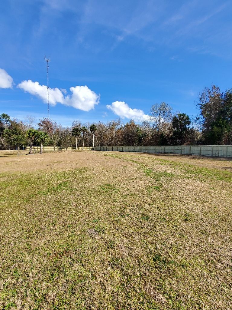 A large grassy field with a fence and trees in the background on a sunny day.