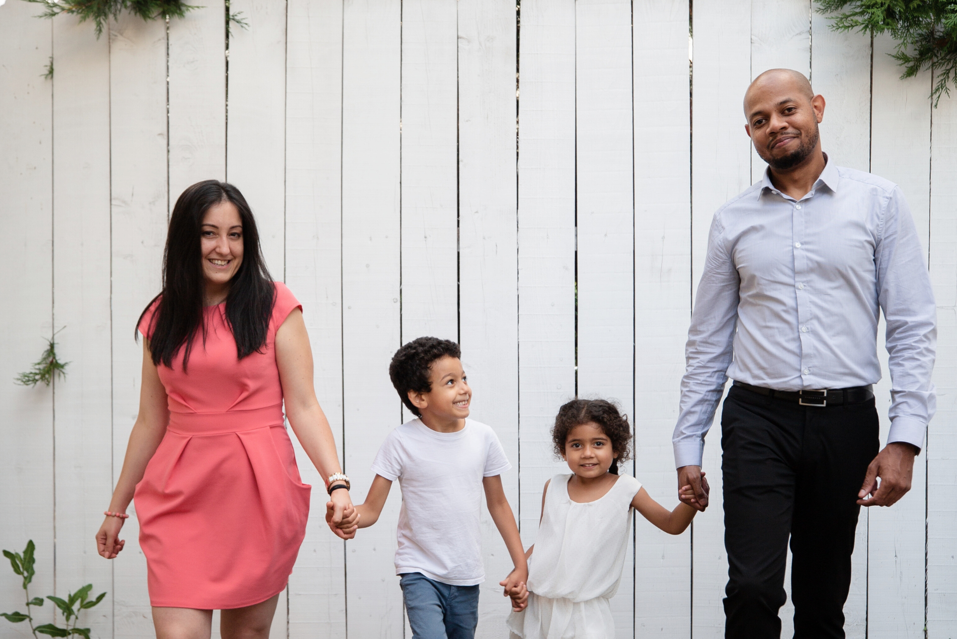 A family is holding hands while walking in front of a white fence.