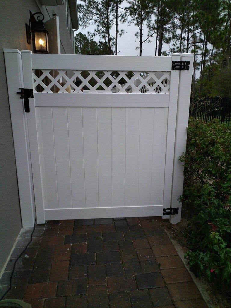 A white gate is sitting on a brick walkway next to a house.