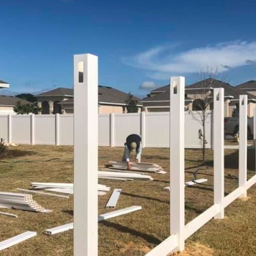 A man is working on a white fence in a backyard.