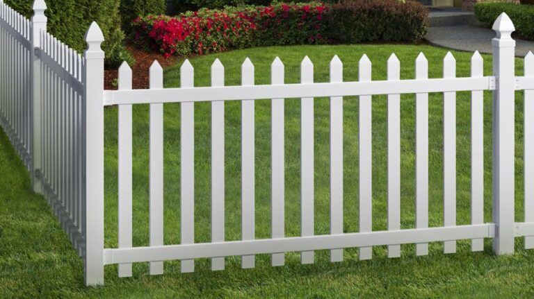 A white picket fence is in the middle of a lush green yard.