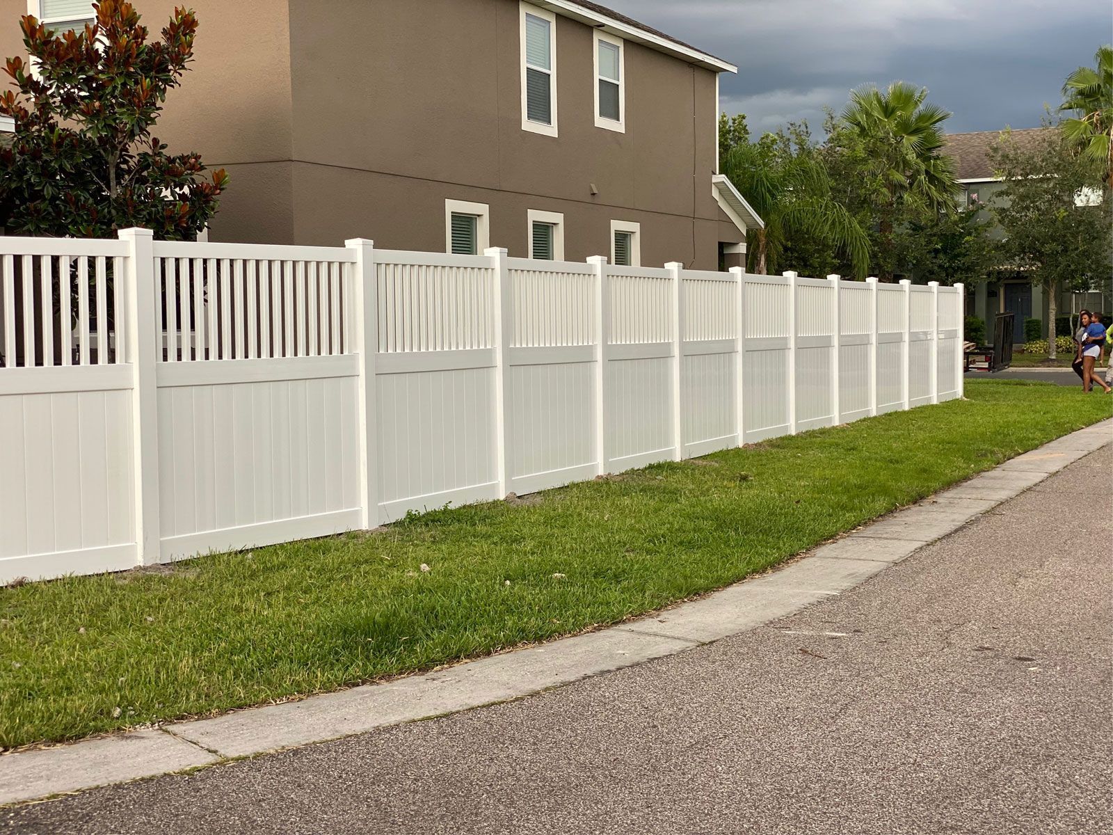 A white fence along the side of a road in front of a house.