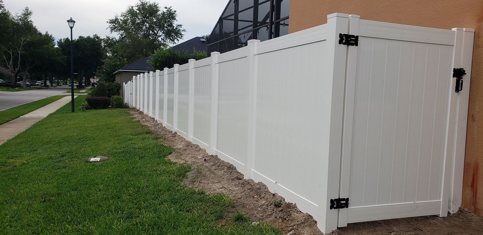 A white fence with a gate is sitting next to a house.