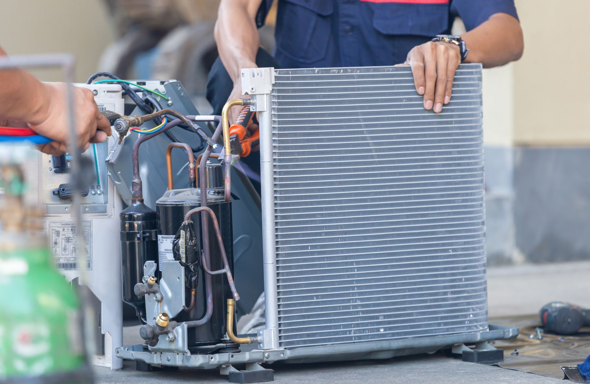 Two technicians repair an air conditioning unit, outdoor setting.
