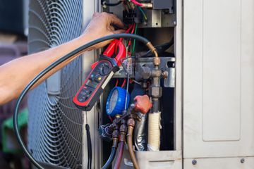 HVAC technician working on an air conditioning unit; using gauges and electrical tools outdoors.