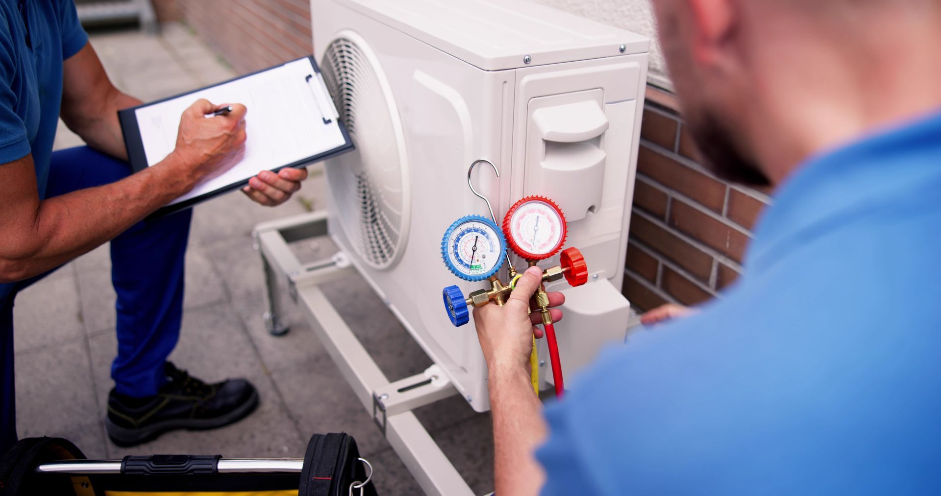 Technicians check pressure gauges on an outdoor air conditioning unit.