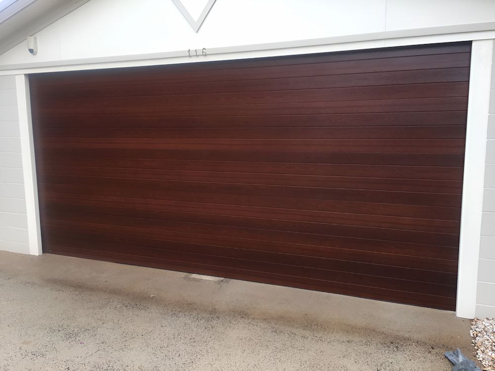 A Large Wooden Garage Door Is Sitting In Front Of A White House — Brunswick Valley Door Centre in Main Arm, NSW