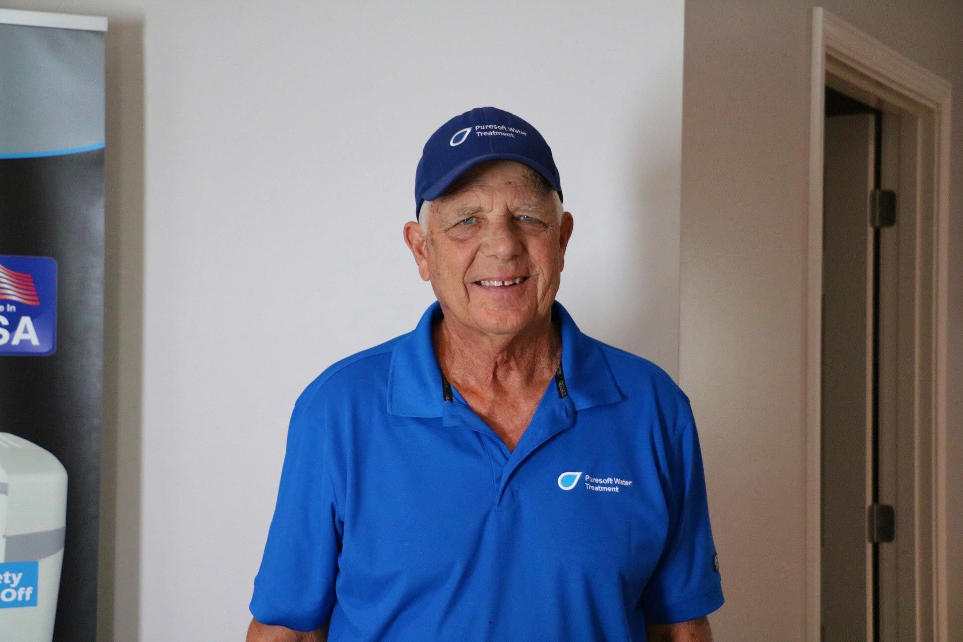 Man in blue polo and cap smiling indoors beside a doorway