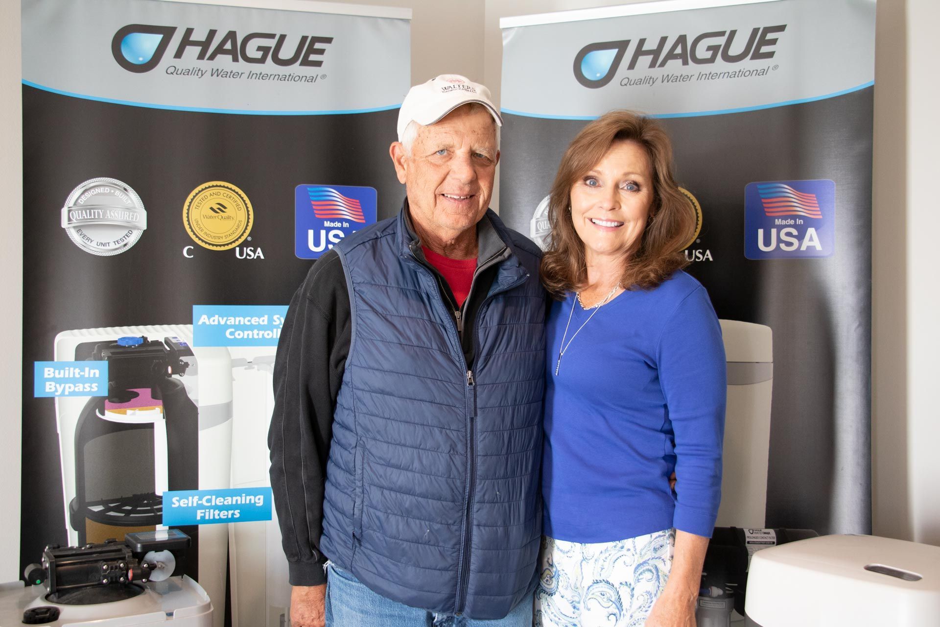 Two people posing in front of Hague display banners at a trade show.