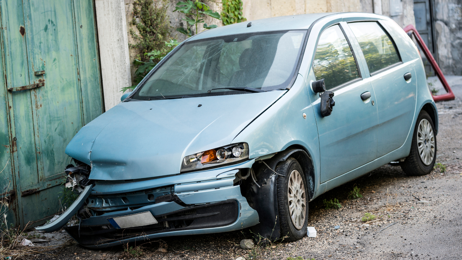 A blue car with a damaged front end is parked in a parking lot.