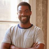 A man with a beard is smiling with his arms crossed in front of a window.