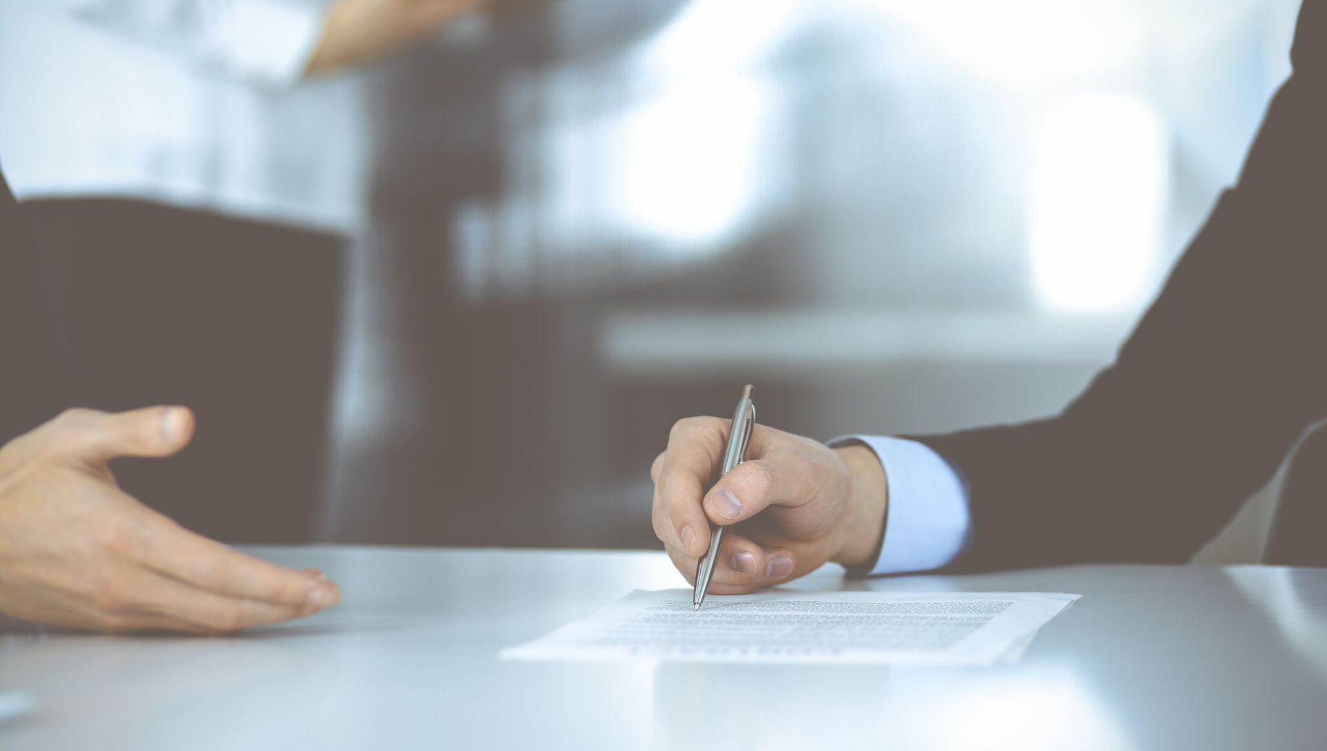 A man is sitting at a table signing a document with a pen.