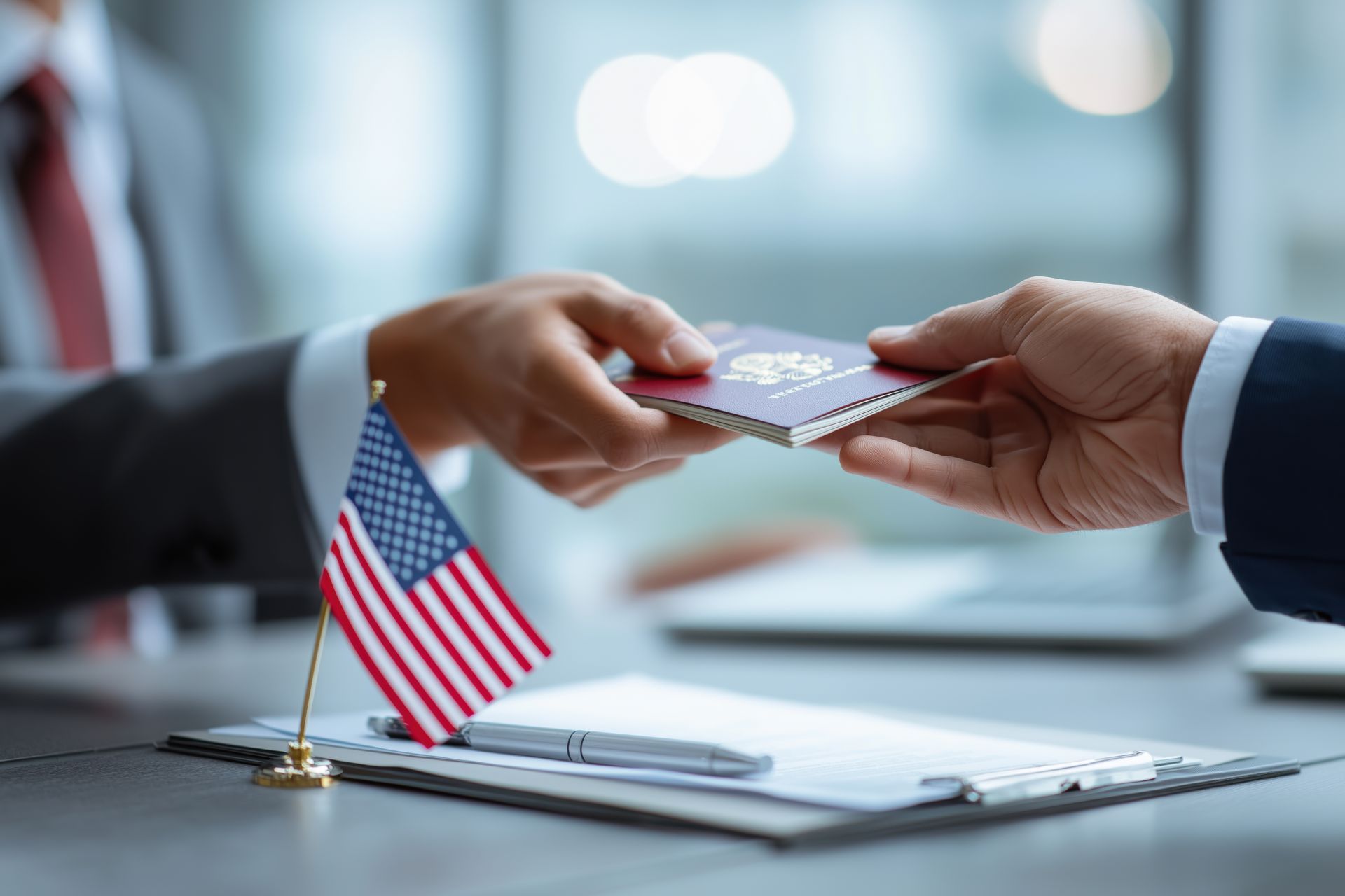 Hands exchanging a passport near an American flag on a desk.