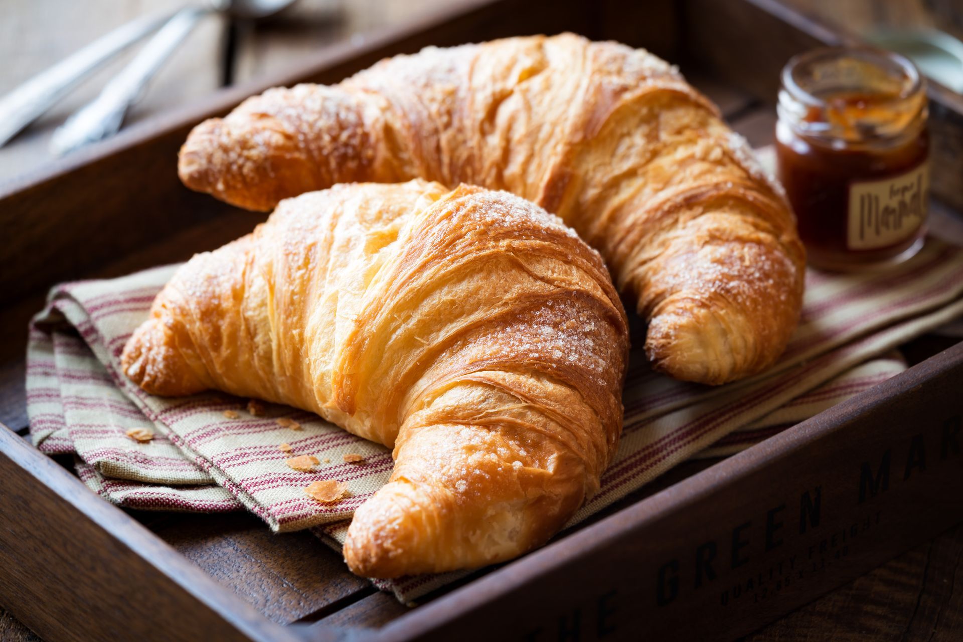 Two croissants are sitting on a wooden tray next to a jar of jam.